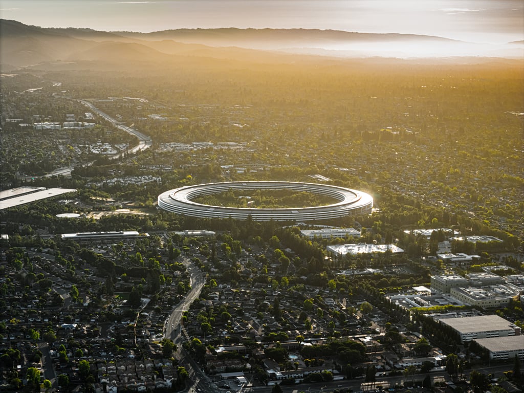 Apple Park i Cupertino sett fra luften i solnedgang, den runde hovedkvarterbygningen omgitt av trær