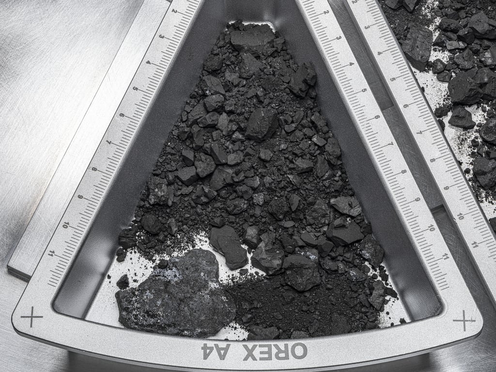 Svarte steiner og støv fra asteroiden Bennu i en metallbeholder med målestokk