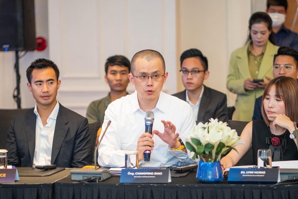 Changpeng Zhao i hvit skjorte snakker i mikrofon ved et konferansebord