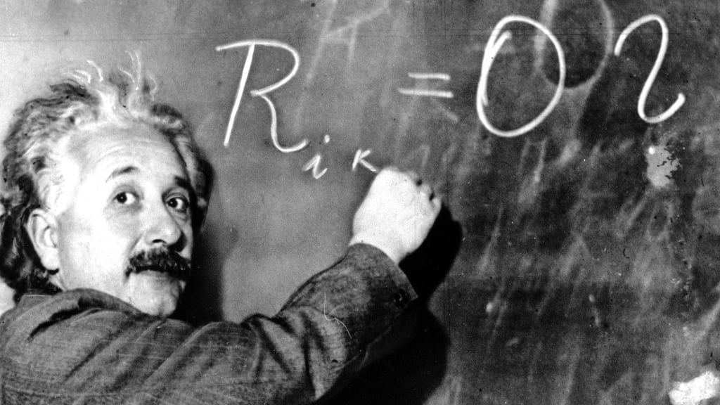 Albert Einstein skriver en formel på en tavle og ser mot kamera