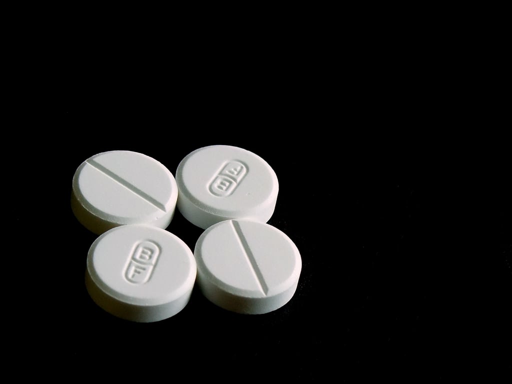 Fire hvite, runde paracetamoltabletter med delestrek, liggende tett sammen på svart bakgrunn
