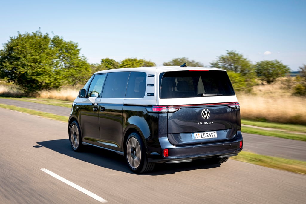 Mørkeblå og hvit Volkswagen ID. Buzz sett bakfra på en solfylt landevei