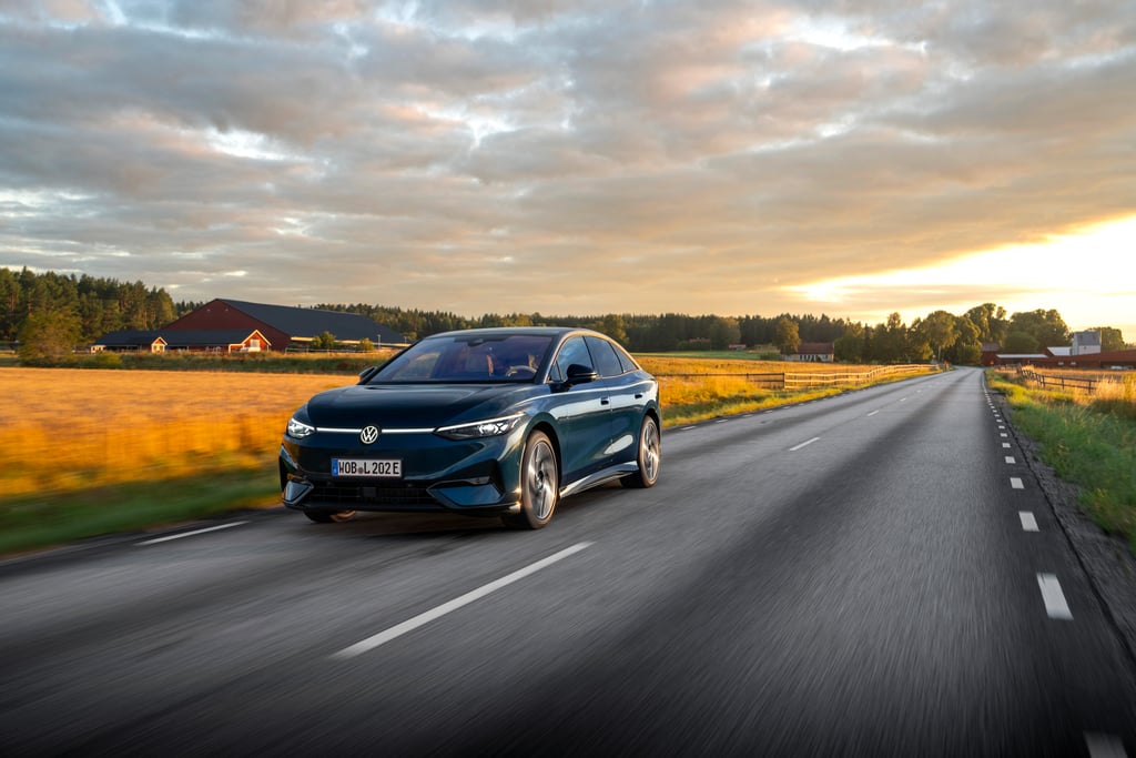 Mørk Volkswagen ID.7 kjører på en landevei forbi gårder og kornåker