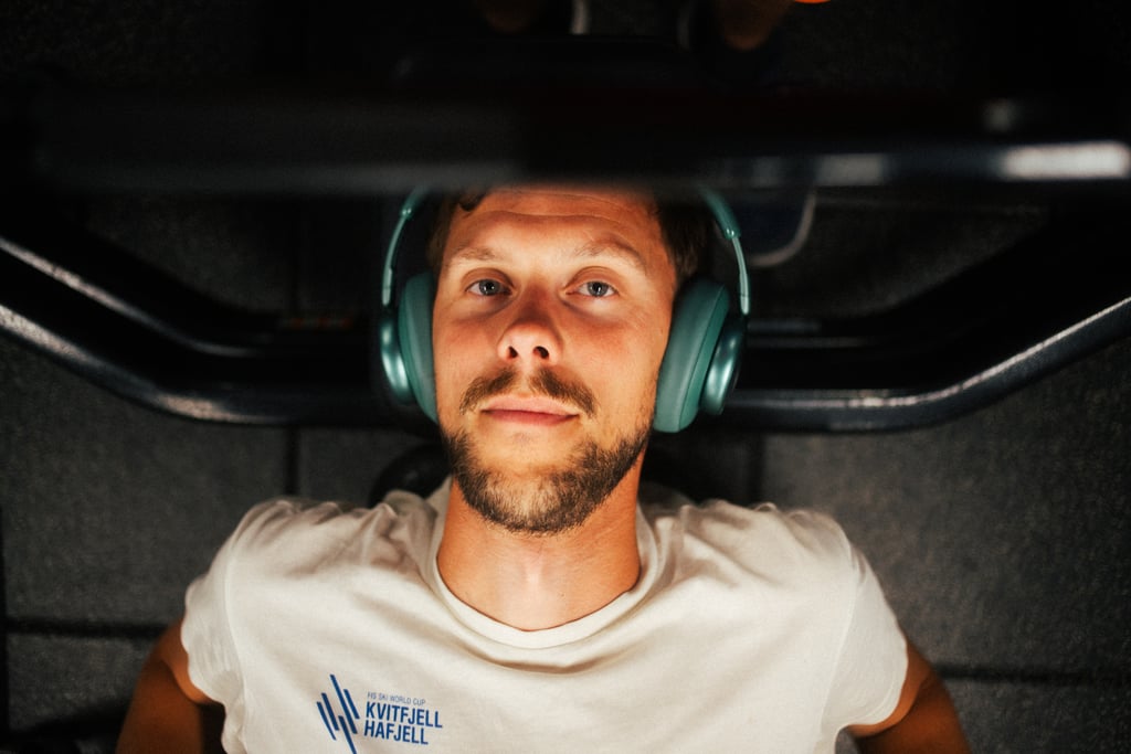 Mann med marinegrønne JBL Live 780NC over ørene i en benkpress på et treningssenter