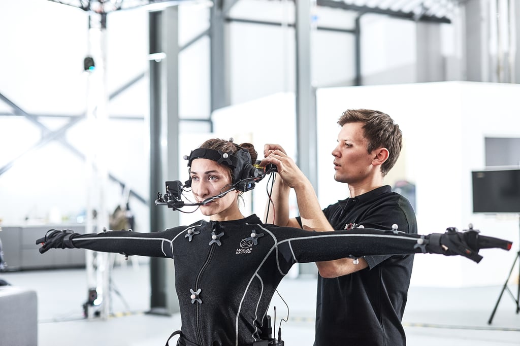Skuespiller i sort mocap-drakt med hvite markører får festet hodekamera i et opptaksstudio