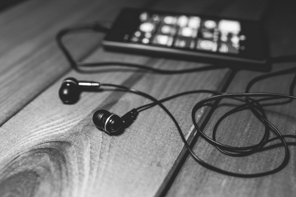 Sorthvitt nærbilde av øreplugger med kabel som ligger på et trebord ved siden av en telefon