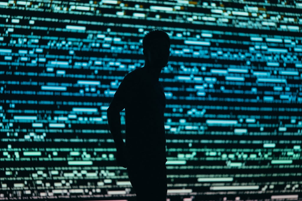 Silhuett av en mann foran en stor skjermvegg full av lysende datalinjer