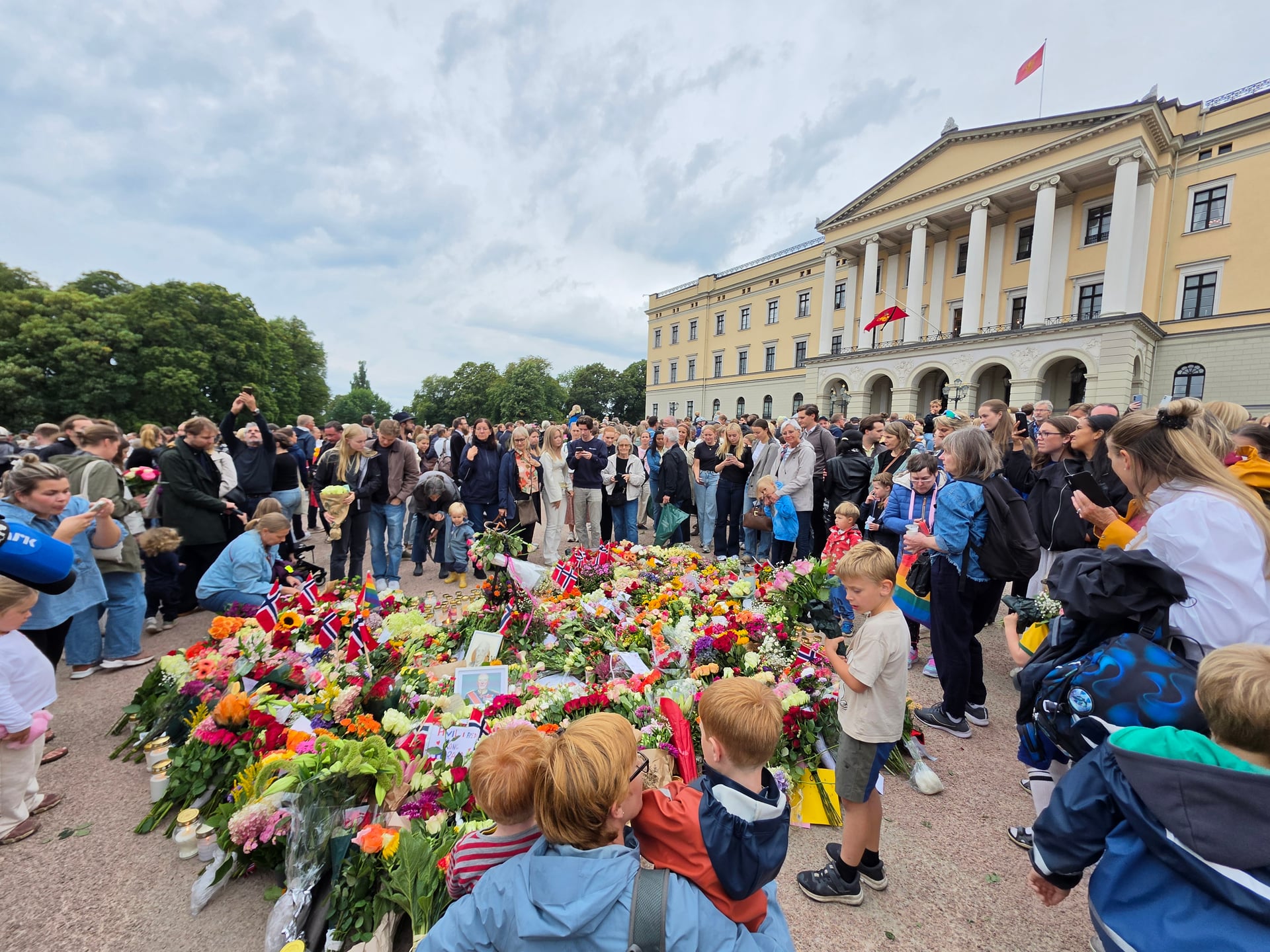 Folkemengde foran Slottet i Oslo med blomsterhav og norske flagg