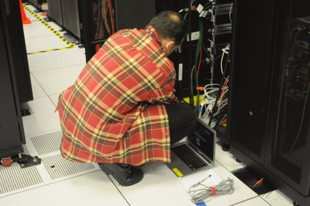 Tekniker sitter på huk med en bærbar PC foran et åpent serverskap i et datasenter