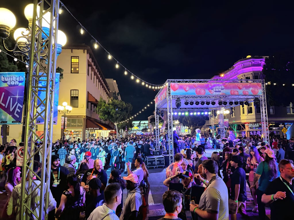 Folkemengde på gaten under TwitchCon om kvelden, med opplyst scene og Twitch-logoer