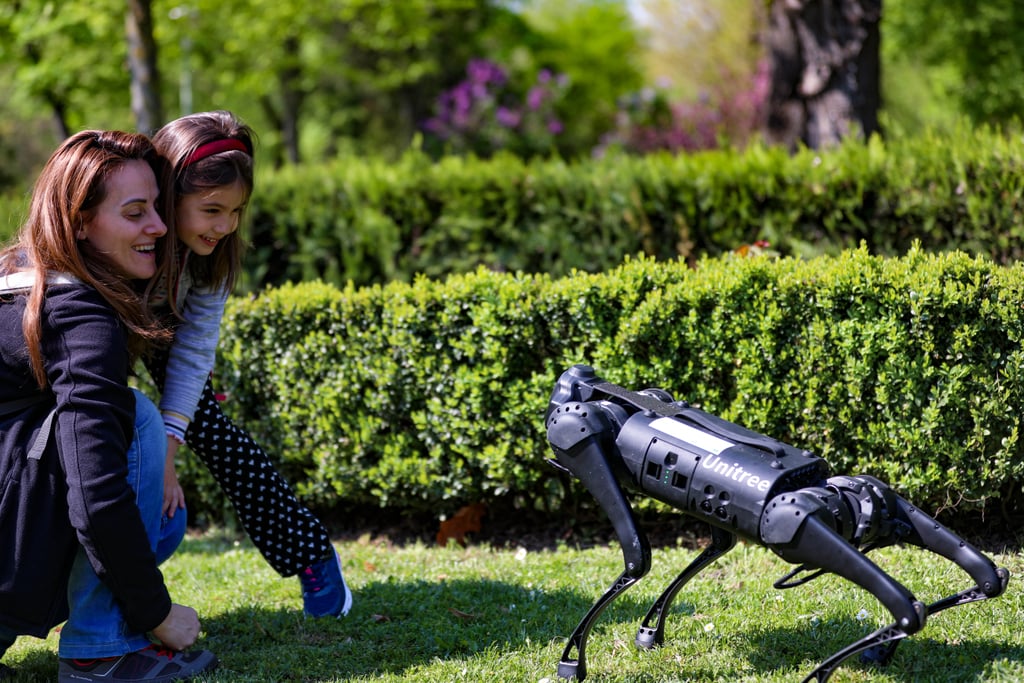 Firbent robot merket Unitree går på en gressplen mens publikum ser på