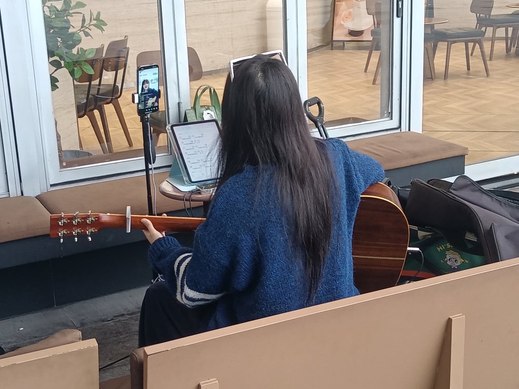 Kvinne spiller gitar foran en mobil som sender direkte på Douyin