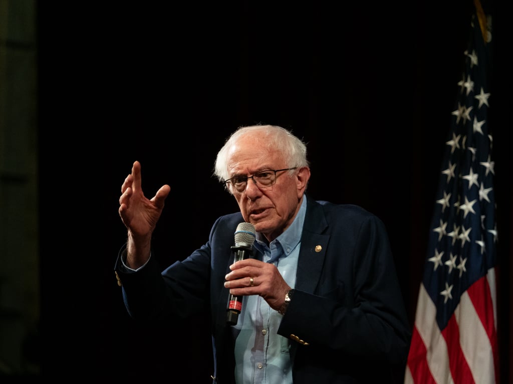 Bernie Sanders snakker i mikrofon foran et amerikansk flagg under et studentmøte ved Stanford