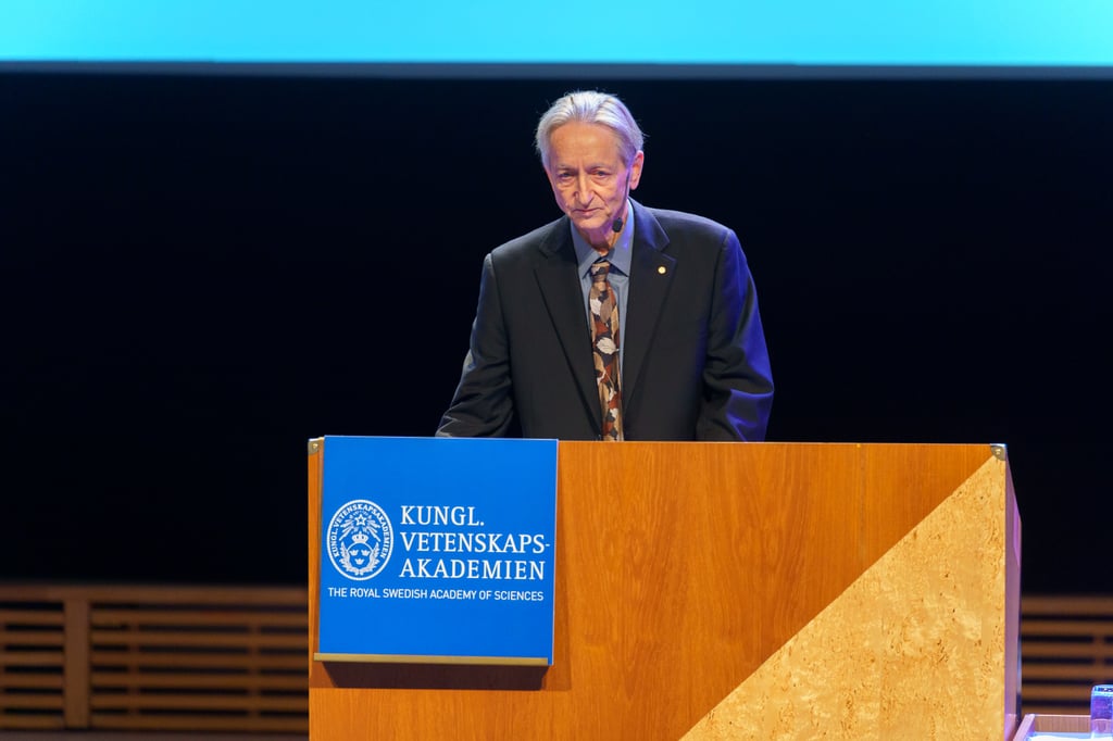 Geoffrey Hinton i mørk dress står bak en talerstol med Vetenskapsakademiens blå logo