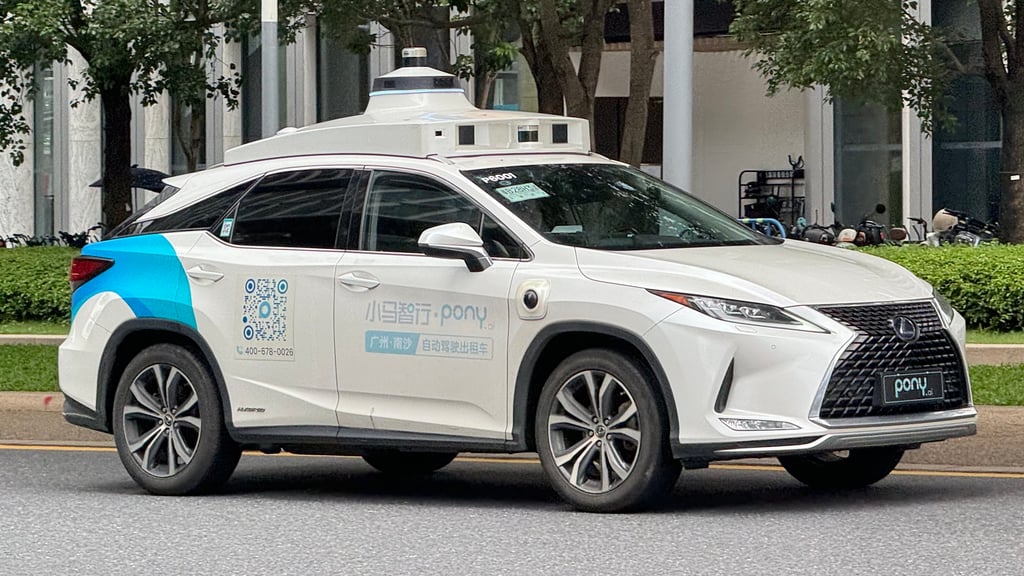 Hvit Pony.ai-robotaxi med sensorer på taket kjører på en gate i Guangzhou