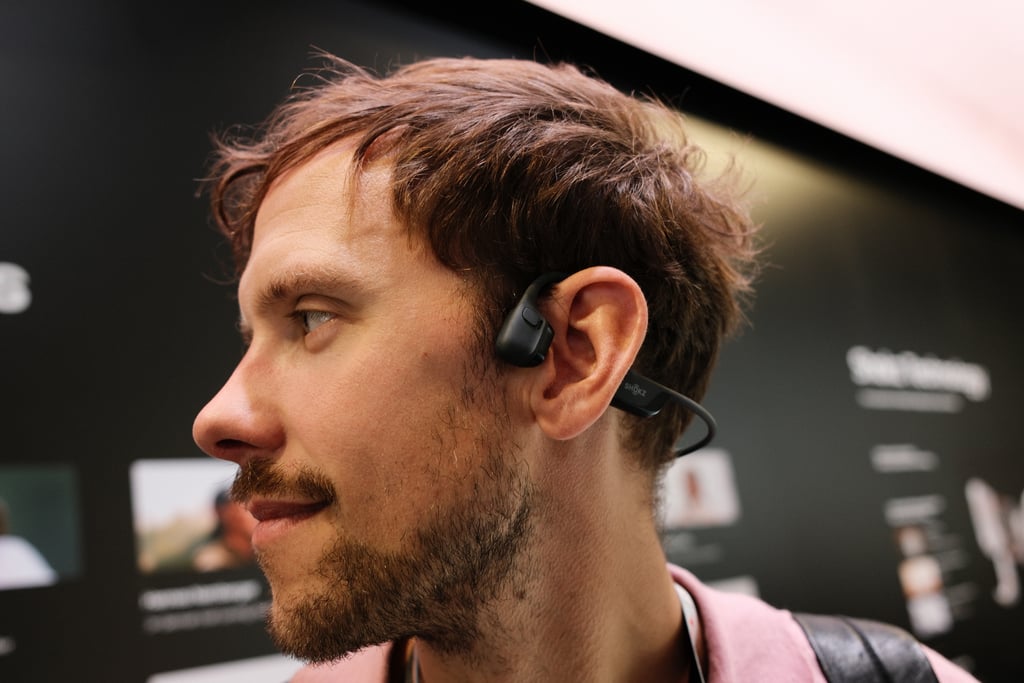 Mann med sort Shokz-hodesett som går bak hodet og hviler foran øret