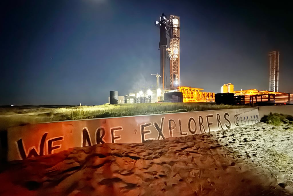 Starship står opplyst på oppskytningsrampen om natten, med en mur i forgrunnen