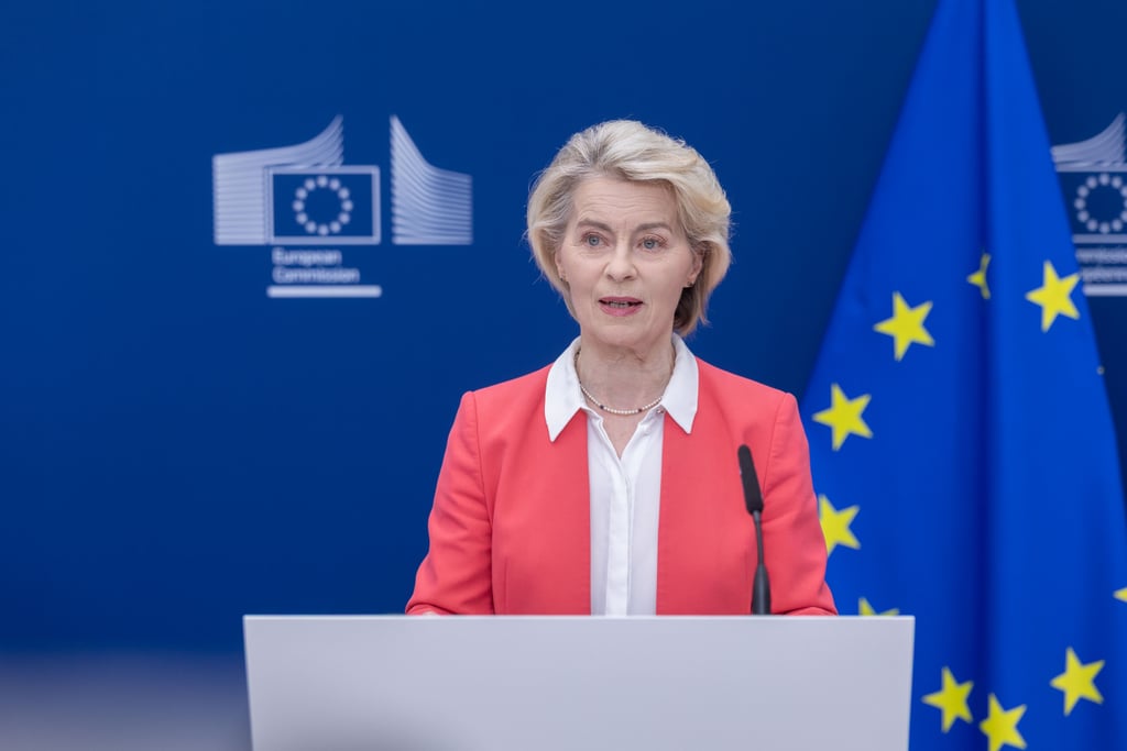 Ursula von der Leyen taler bak en talerstol foran Europakommisjonens logo og EU-flagget