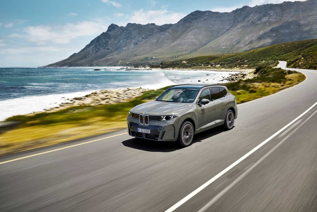 BMW iX5 kjører langs en kystvei med fjell i bakgrunnen