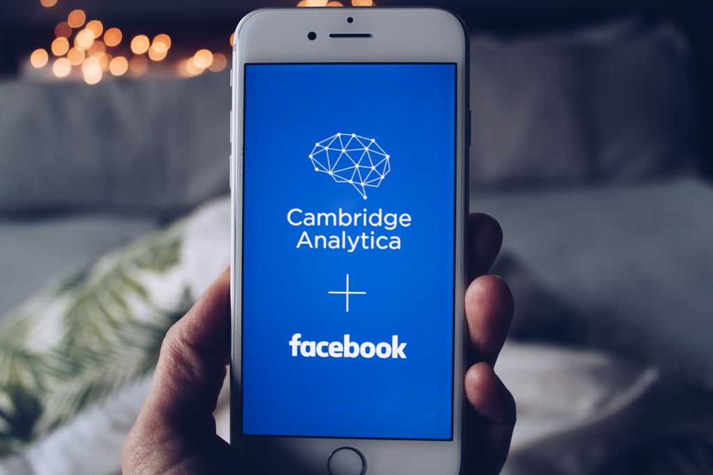En hånd holder en mobil med logoene til Cambridge Analytica og Facebook på skjermen