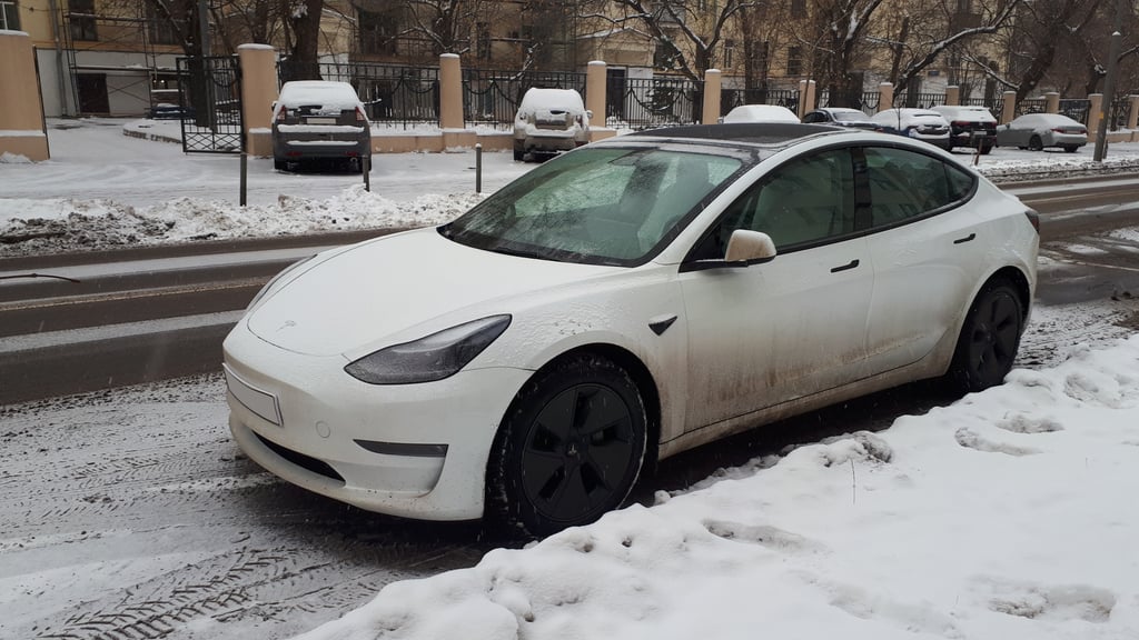 En hvit elbil med sneslaps på lakken står parkert langs en vei om vinteren