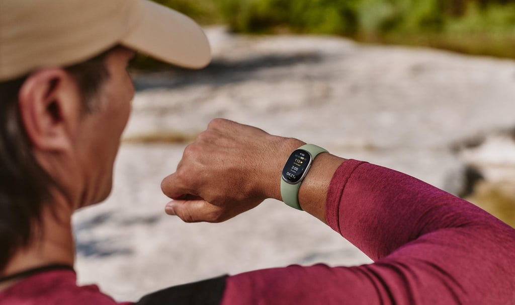En mann med caps ser på et grønt Fitbit Edge på håndleddet, ute ved et svaberg