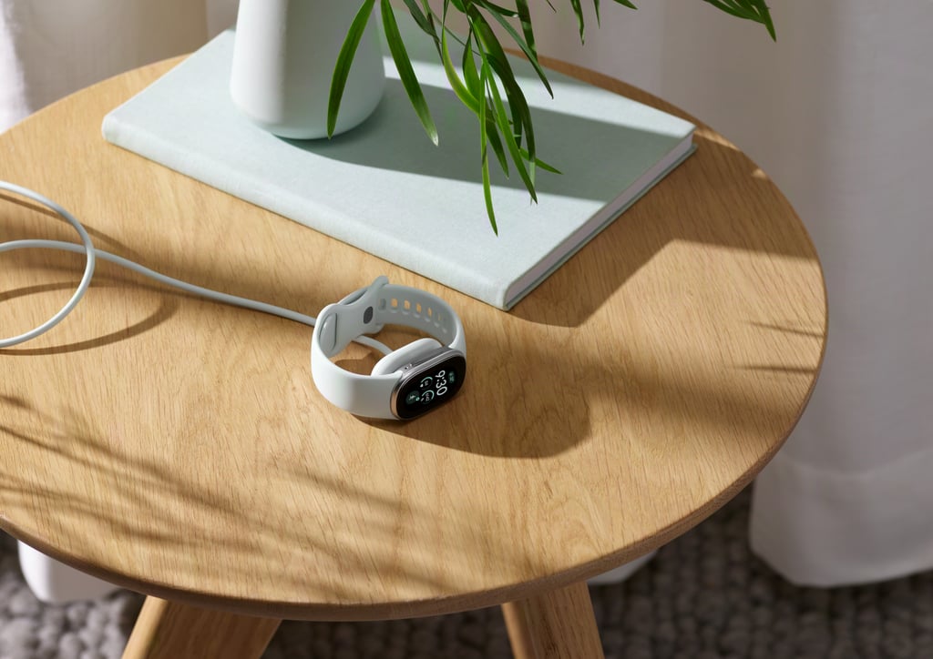 Hvit Fitbit Edge ligger til lading på et rundt trebord ved siden av en plante