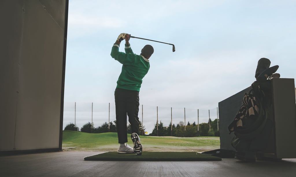 Golfspiller i grønn genser slår ut fra en matte på en driving range