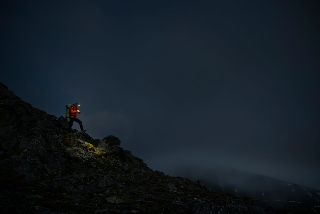 Løper med hodelykt på vei opp en steinete fjellside i mørket