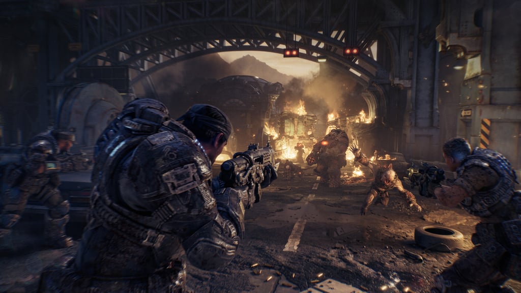 Marcus Fenix sikter med geværet mot monstre som stormer frem mellom brennende vrak under en stålbro
