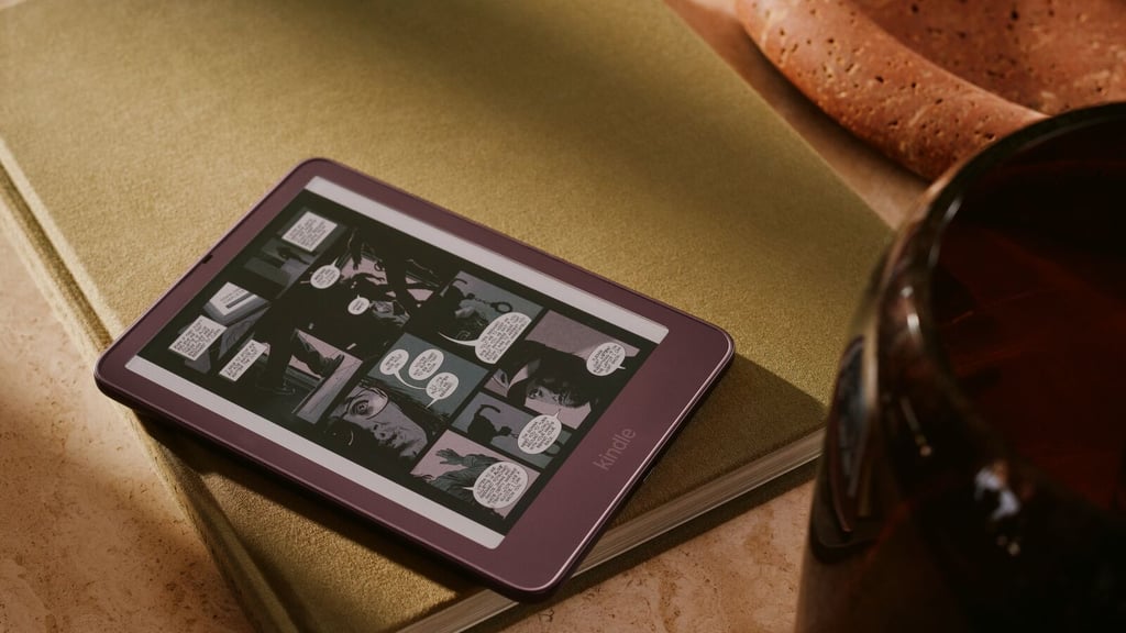 Vinrød Kindle Colorsoft med en tegneserieside i farver på skjermen, liggende på en grønn bok