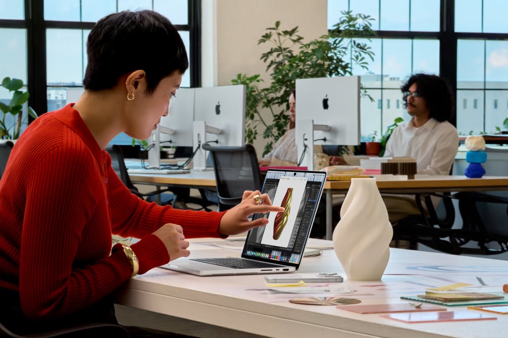 En person ved et skrivebord berører skjermen på nye MacBook Pro