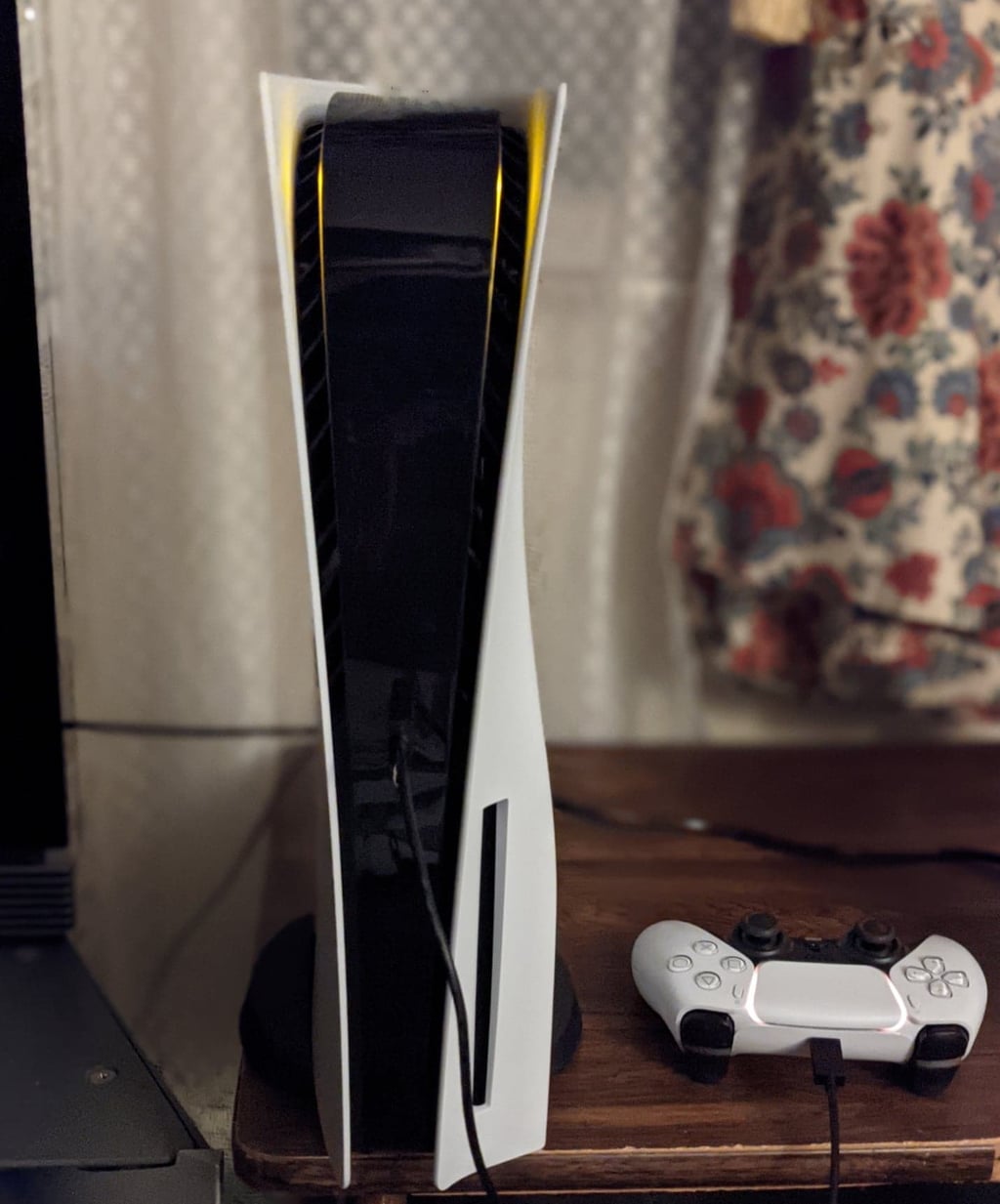 Hvit PlayStation 5 stående på en kommode med en DualSense-kontroller