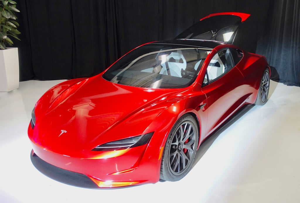 Rød Tesla Roadster-prototype med åpent tak, sett skrått forfra mot en mørk bakvegg