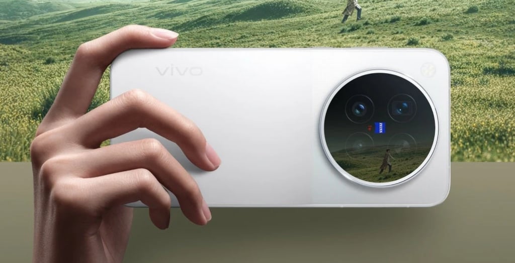 En hånd holder en hvit Vivo X500 foran et grønt landskap