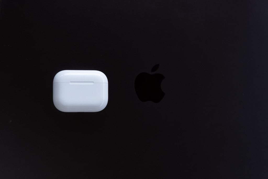 AirPods Pro 3-etui ved siden av Apple-logoen på et mørkt MacBook-lokk