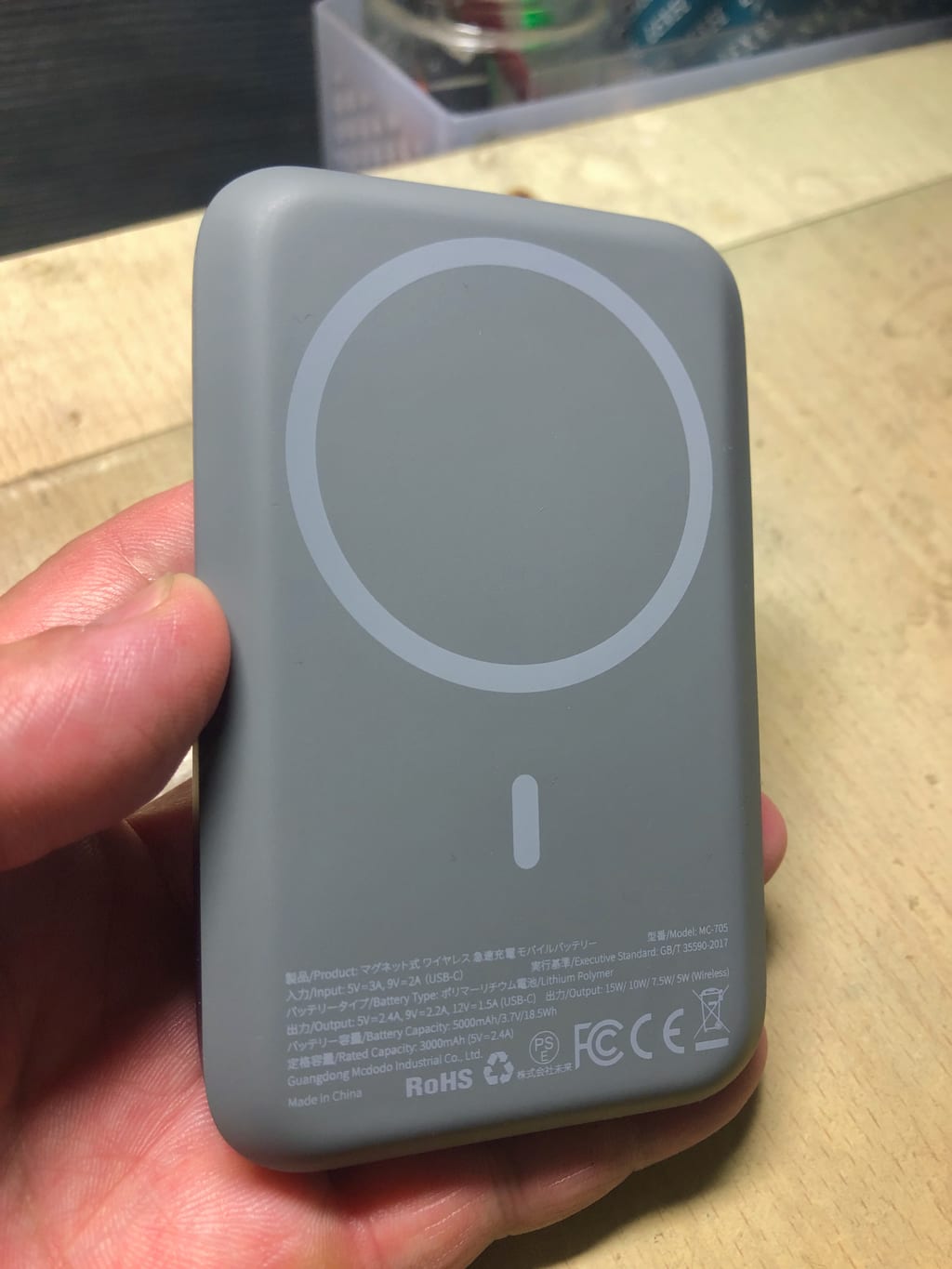 Hånd som holder et grått magnetisk batteri med laderingen synlig på baksiden.