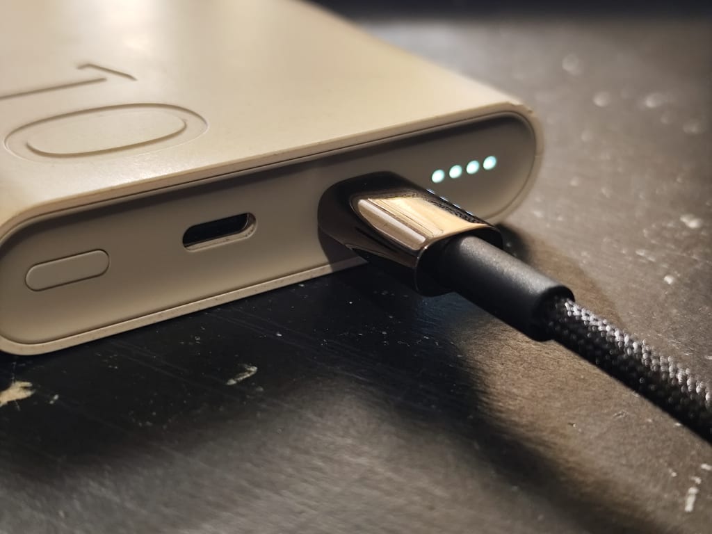 Nærbilde av en USB-C-kabel koblet til en powerbank med fire grønne ladelys.