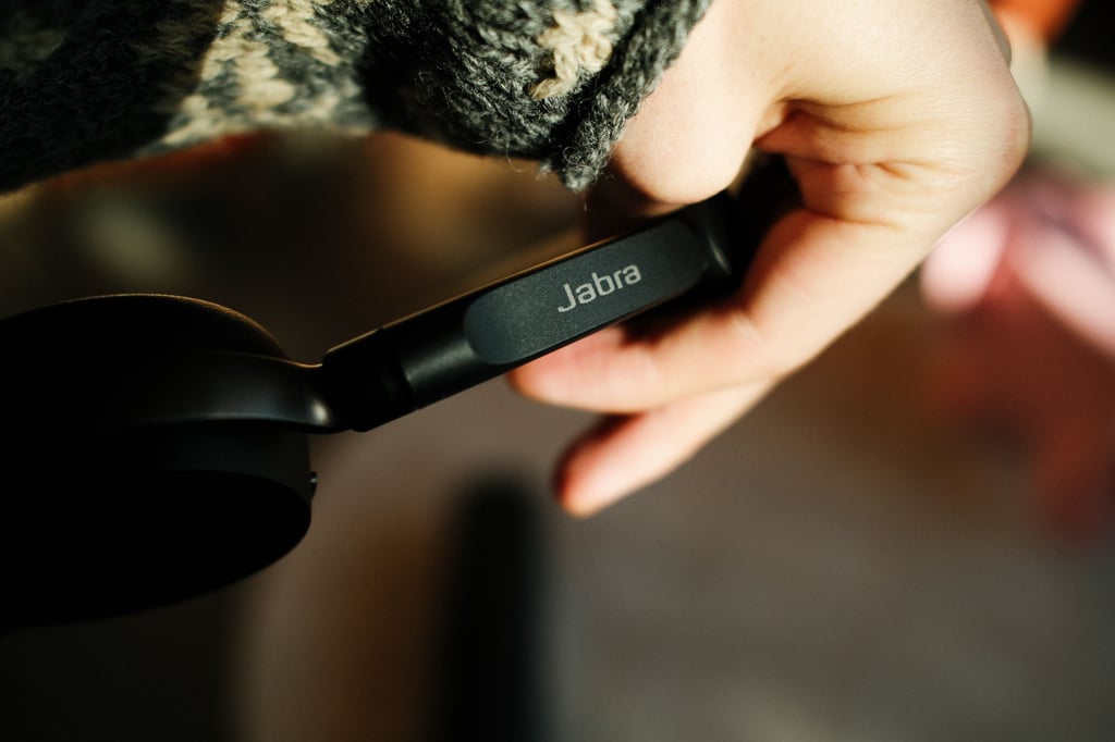 Jabra-logoen på hengslet til Jabra Evolve3 65 Flex, med en strikkegenser bak
