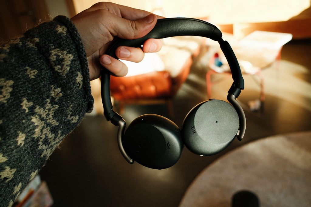 Jabra Evolve3 65 Flex holdt i hånda, med en stue i bakgrunnen