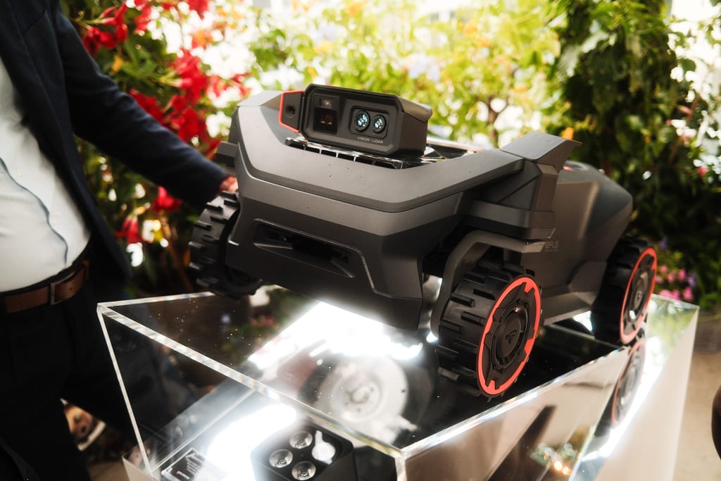 Robotgressklipperen Navimow H5 Pro på en speilsokkel med sensormodul merket Vision Lidar på toppen, fotografert mellom blomster på en takterrasse