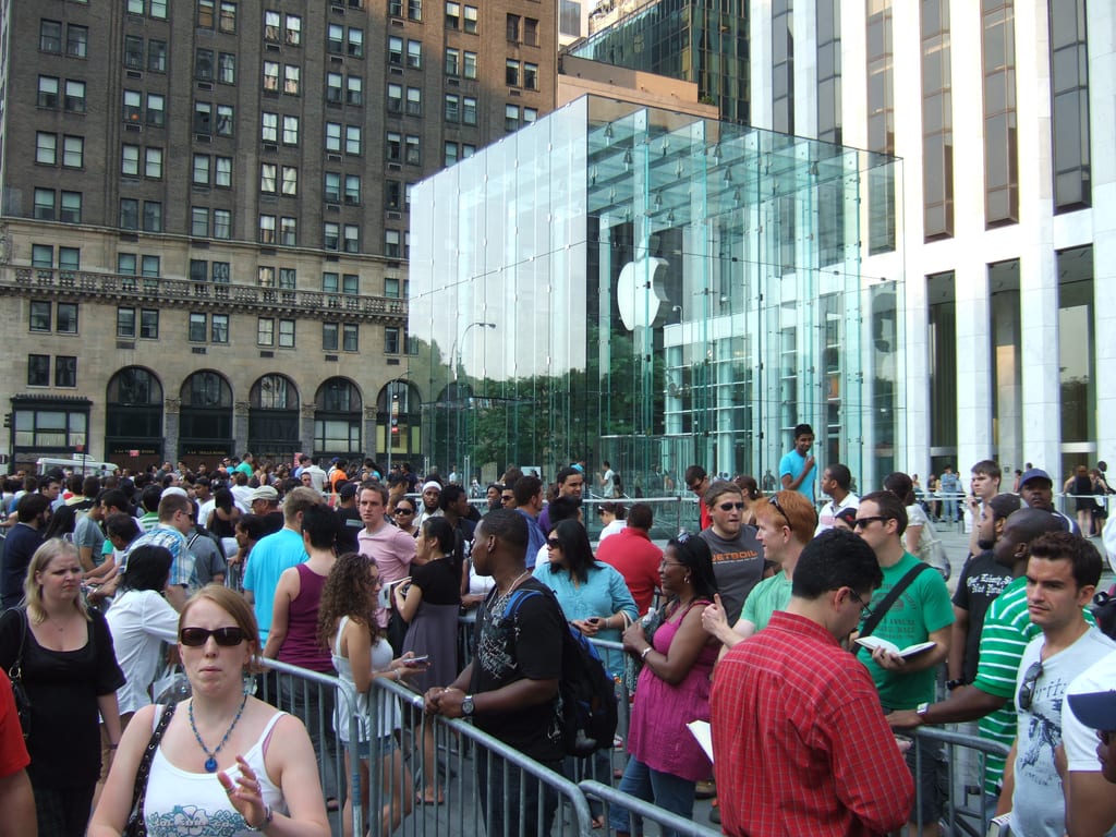 Lang kø av folk bak sperringer foran glasskuben til Apple Store på Fifth Avenue i New York.