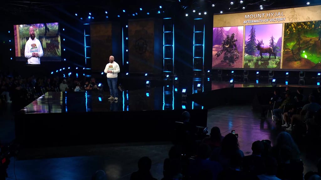 Oversikt over BlizzCon-scenen under What's Next-panelet: En utvikler i hvit genser, storskjermen viser «Mount Hyjal – Aftermath of Victory» med tre bilder fra sonen