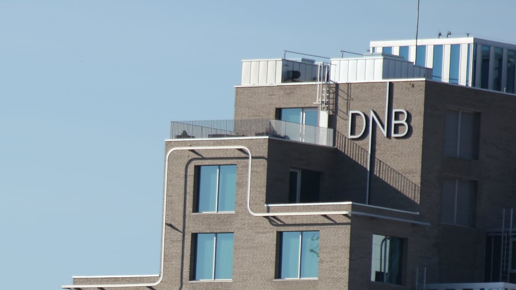 DNB-skiltet på toppen av bankens hovedkontor i Bjørvika, Oslo, mot blå himmel