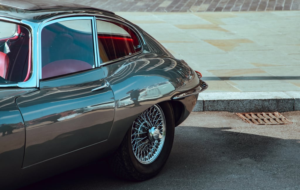 Bakre halvdel av en grågrønn Jaguar E-Type med eikefelger og rødt skinninteriør