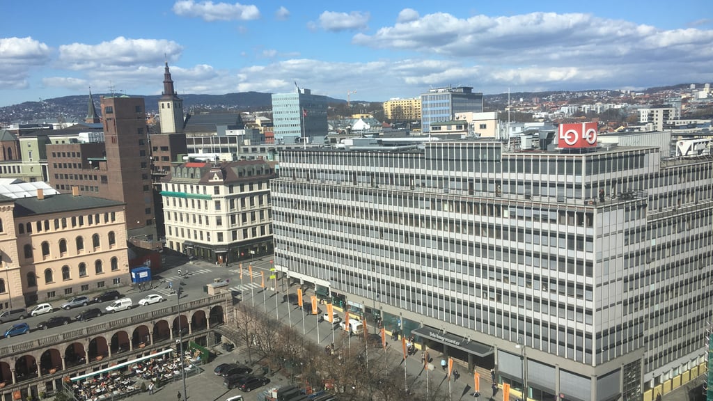 Høyt kontorbygg med LO-logo på taket ved Youngstorget i Oslo, sett ovenfra en solrik dag