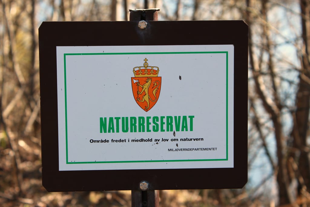 Brunt skilt med riksløven og teksten Naturreservat foran uskarp skog
