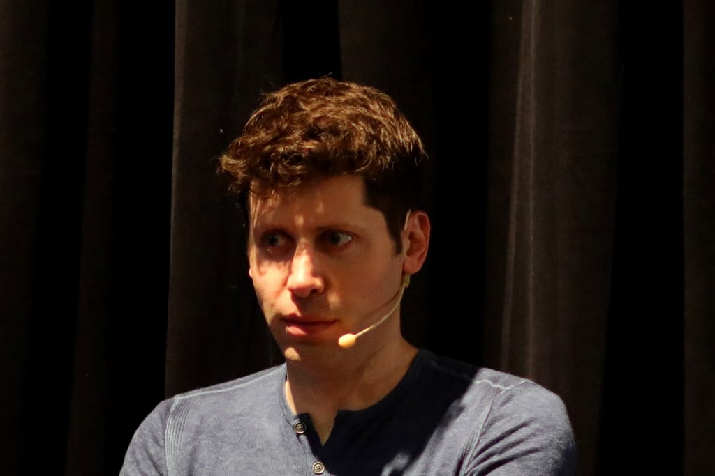 Sam Altman med hodemikrofon foran et mørkt sceneteppe. Han ser til siden.