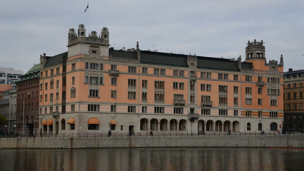 Rosenbad, en laksefarget bygård med tårn og svensk flagg, sett over vannet i Stockholm