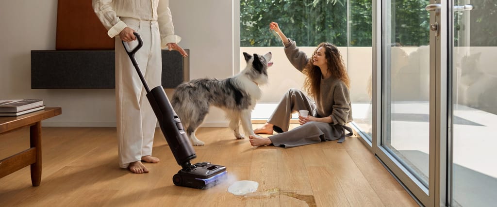 Den stående våt- og tørrstøvsugeren Roborock F25 Ultra Steam Gen 2 i bruk på et tregulv med søl, hund og to personer i en stue